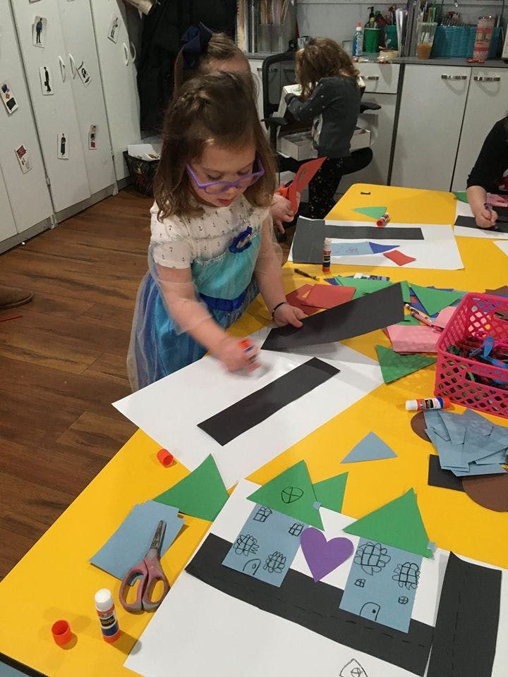 Child in glasses gluing paper onto a craft project at a table