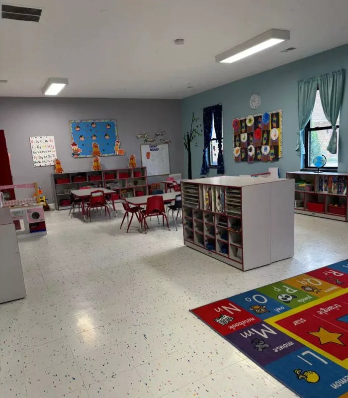 Empty classroom with small tables and chairs, storage units, and an alphabet rug