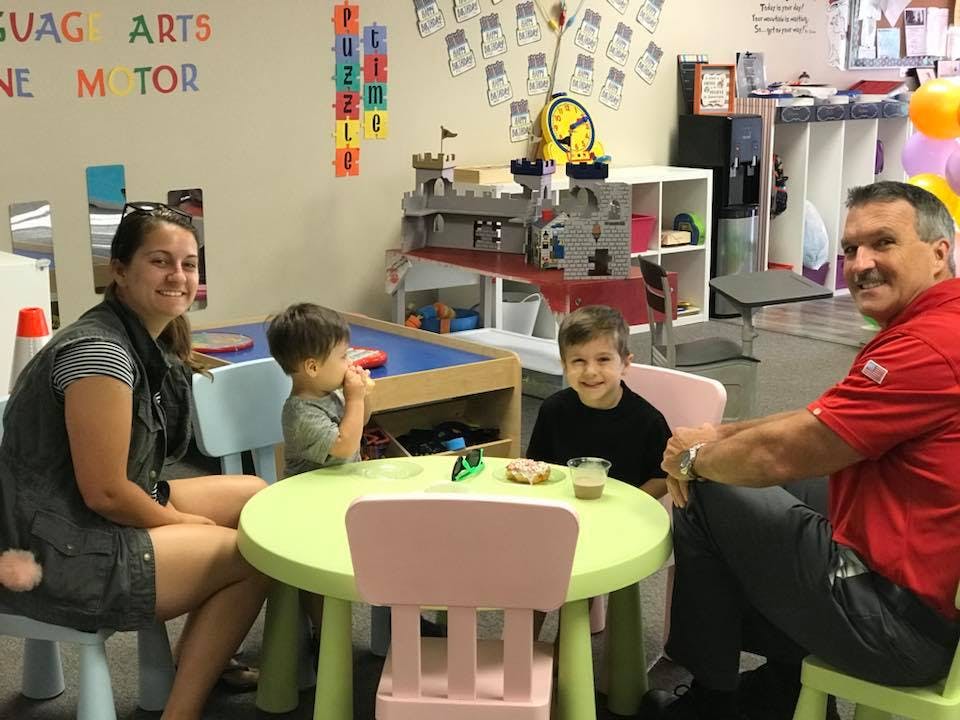 Two adults and two children sitting at a small table in a classroom