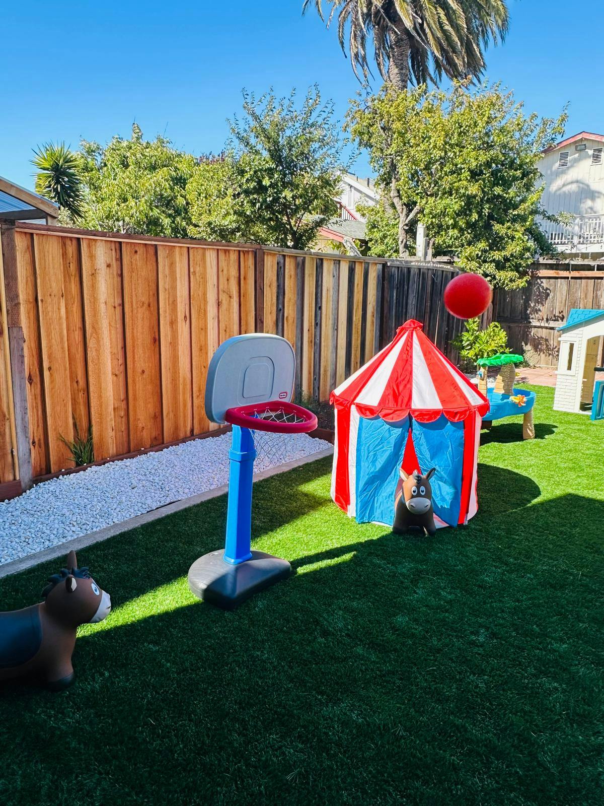 Backyard with a small basketball hoop, red and white tent, and toys on a green lawn
