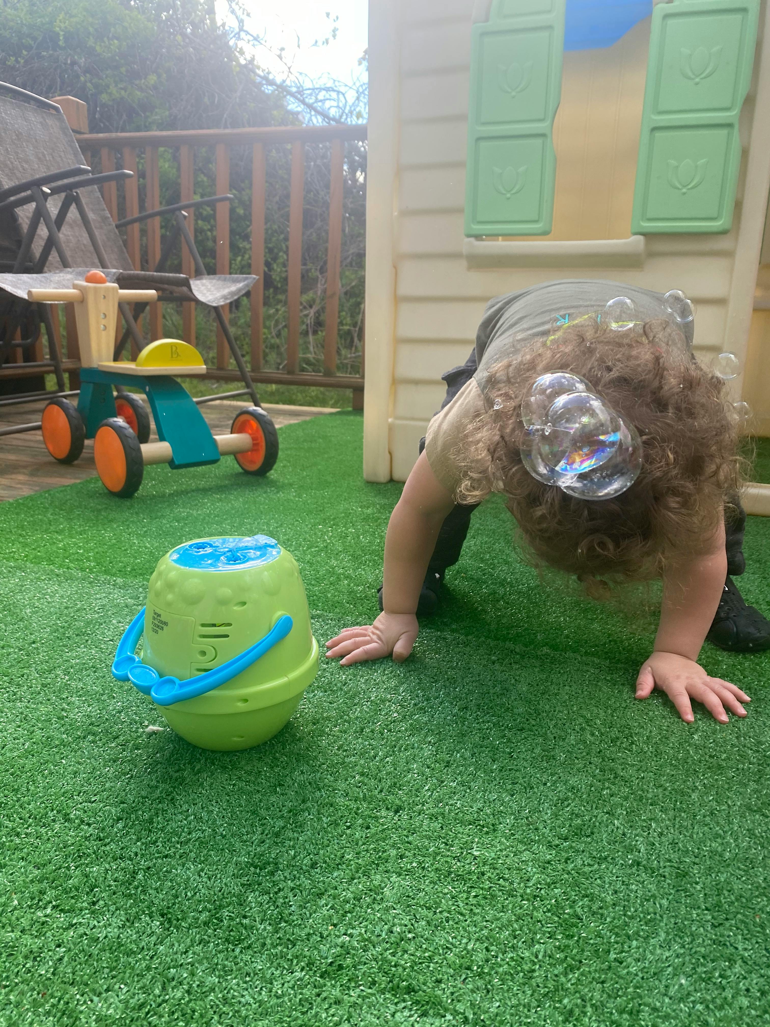 Child on hands and knees near a bubble machine with bubbles in hair