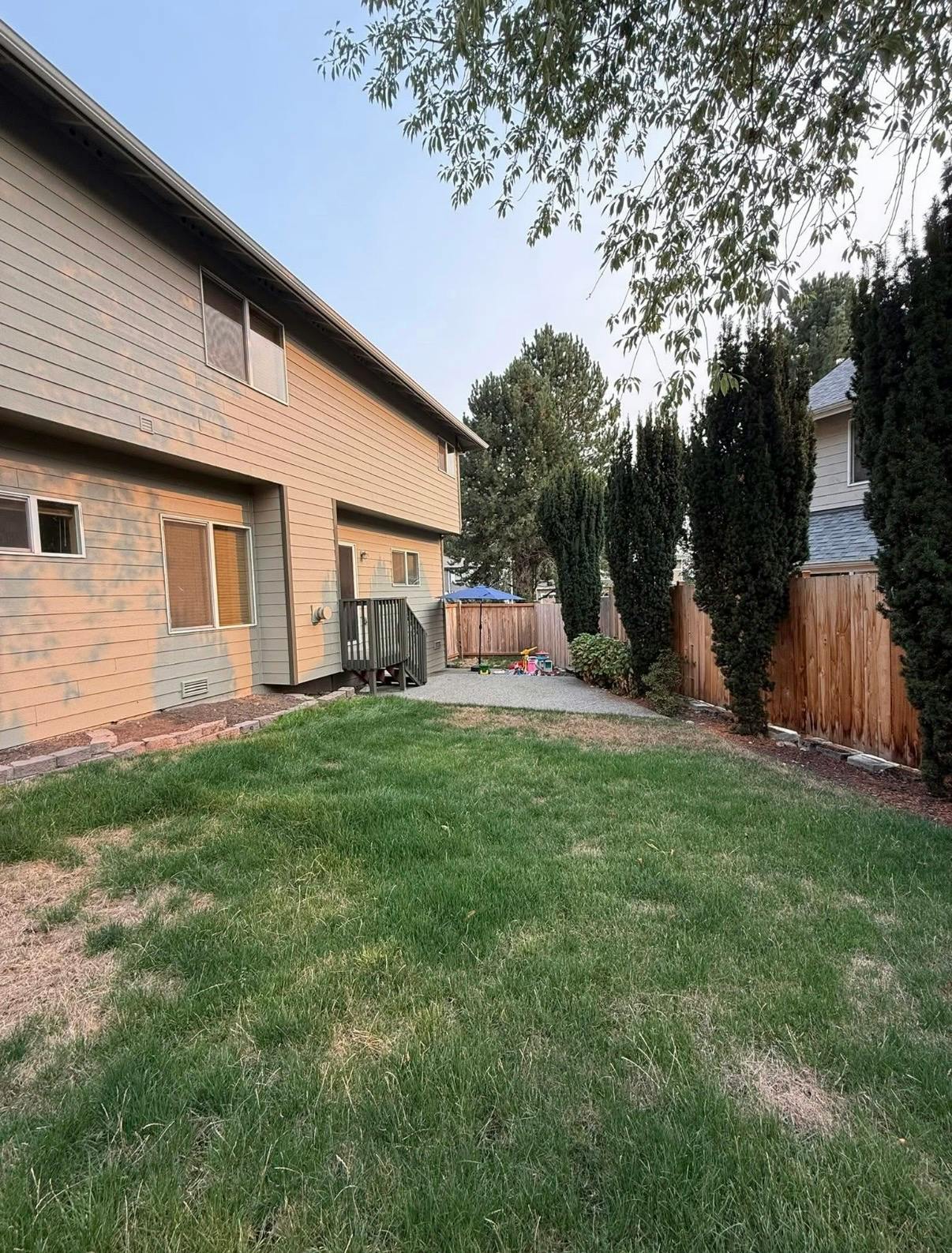Backyard with a house, grass, a fence, and tall trees