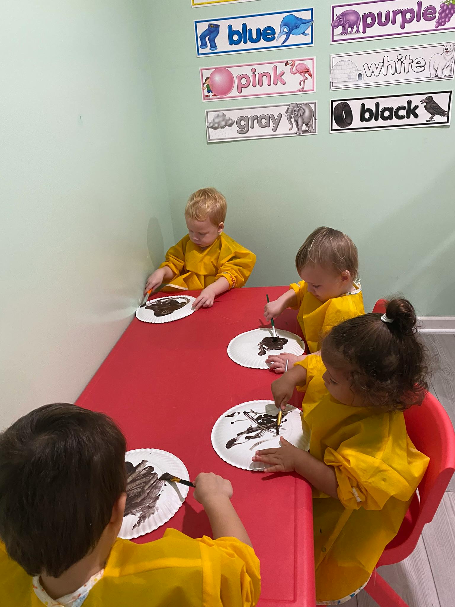 Four children painting on paper plates at a red table