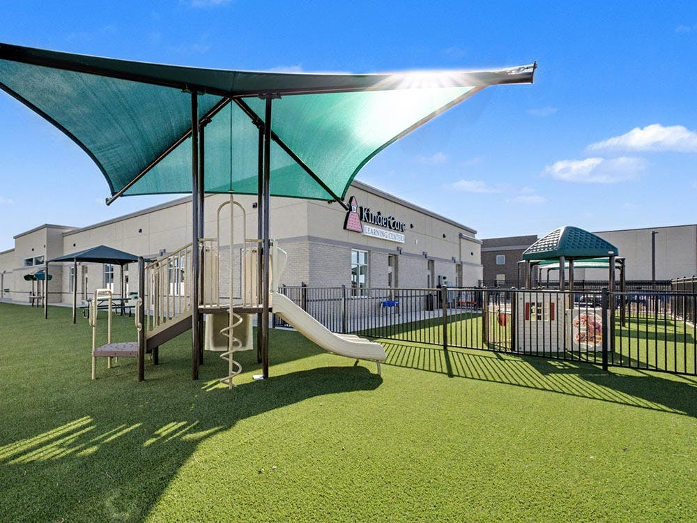 Outdoor playground with artificial turf, play structure, and building in background