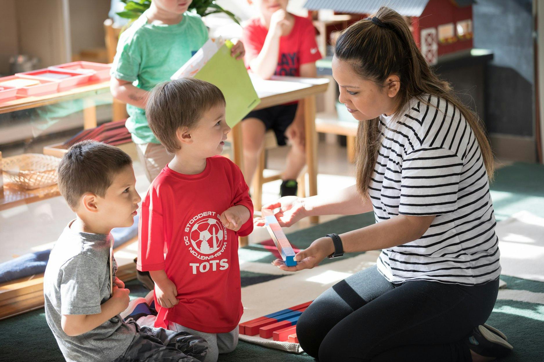 Adult showing two children a small object in a classroom