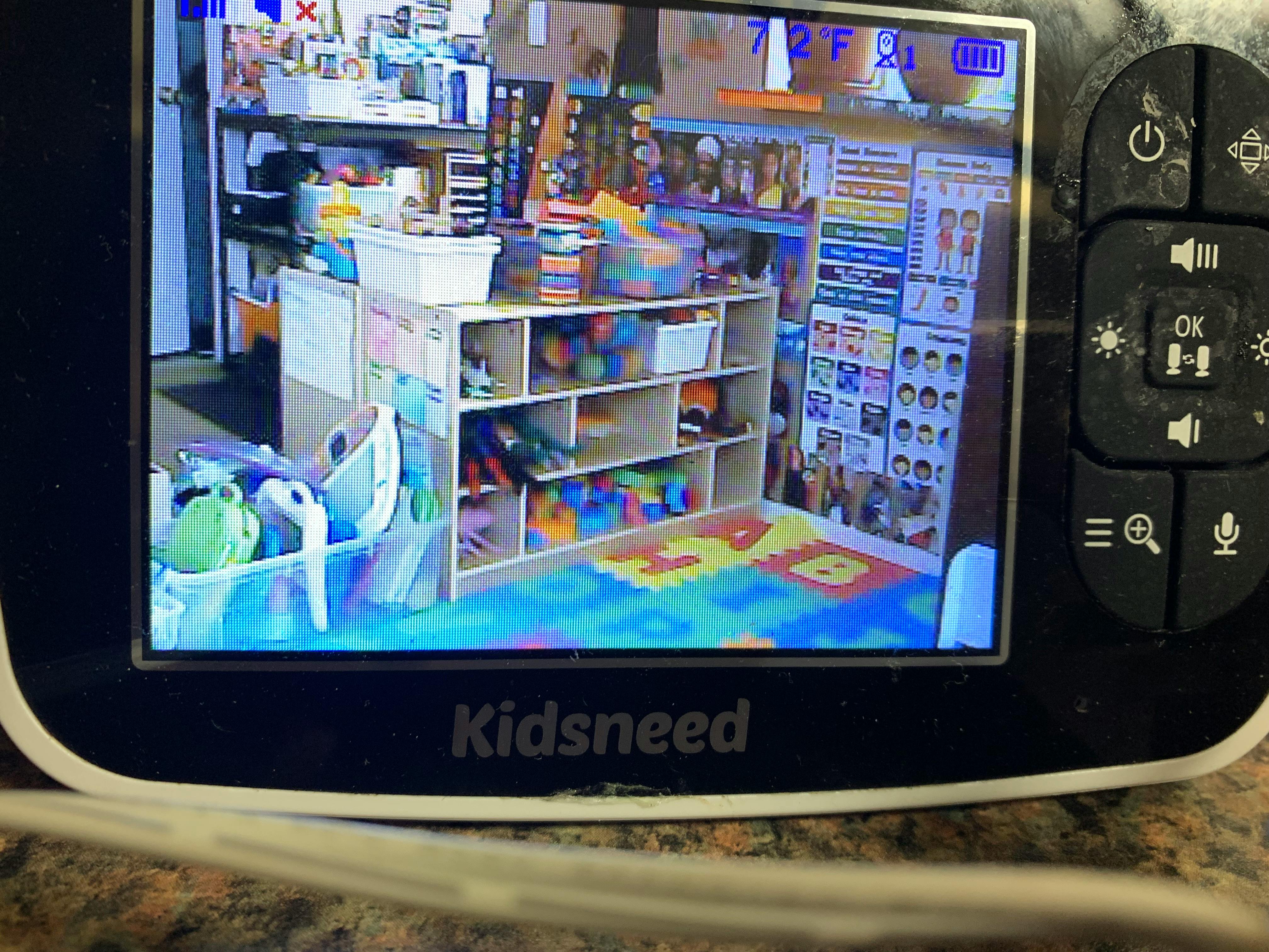 Baby monitor screen showing a playroom with shelves of toys and a colorful mat