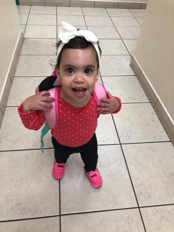 Child wearing a white bow headband and a pink backpack
