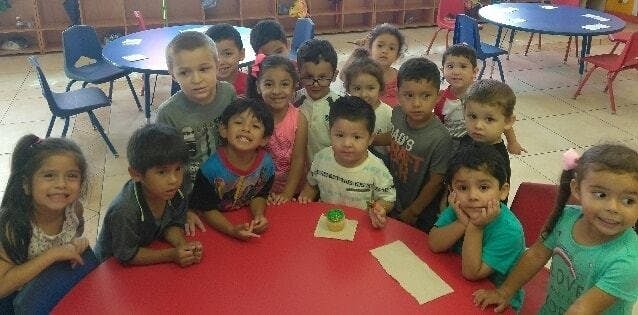 Group of children gathered around a red table in a classroom