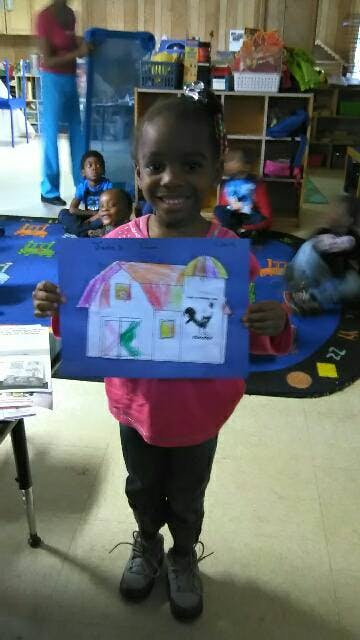 Child holding up a drawing of a barn and silo