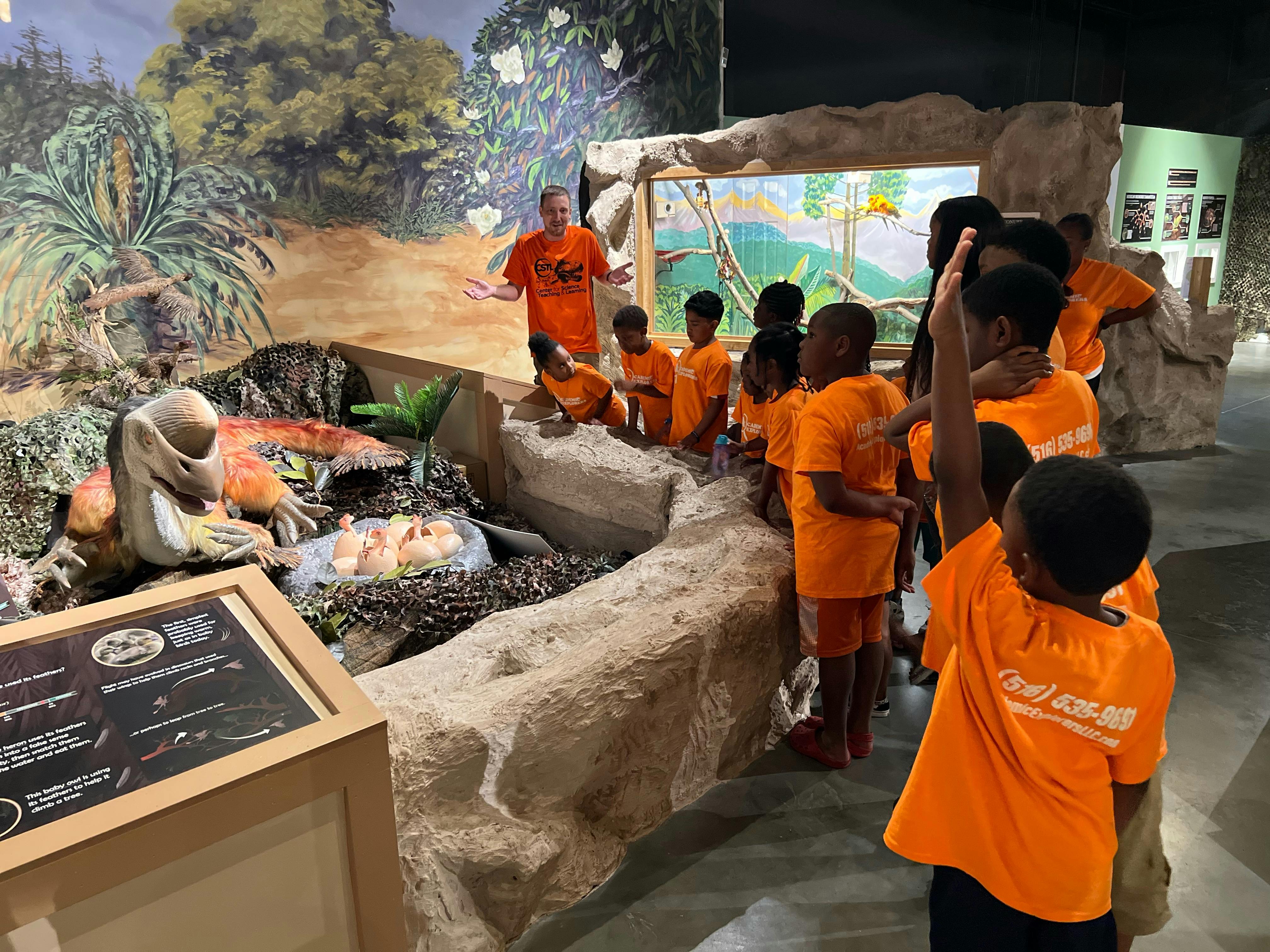Person speaking to children in orange shirts at a museum exhibit
