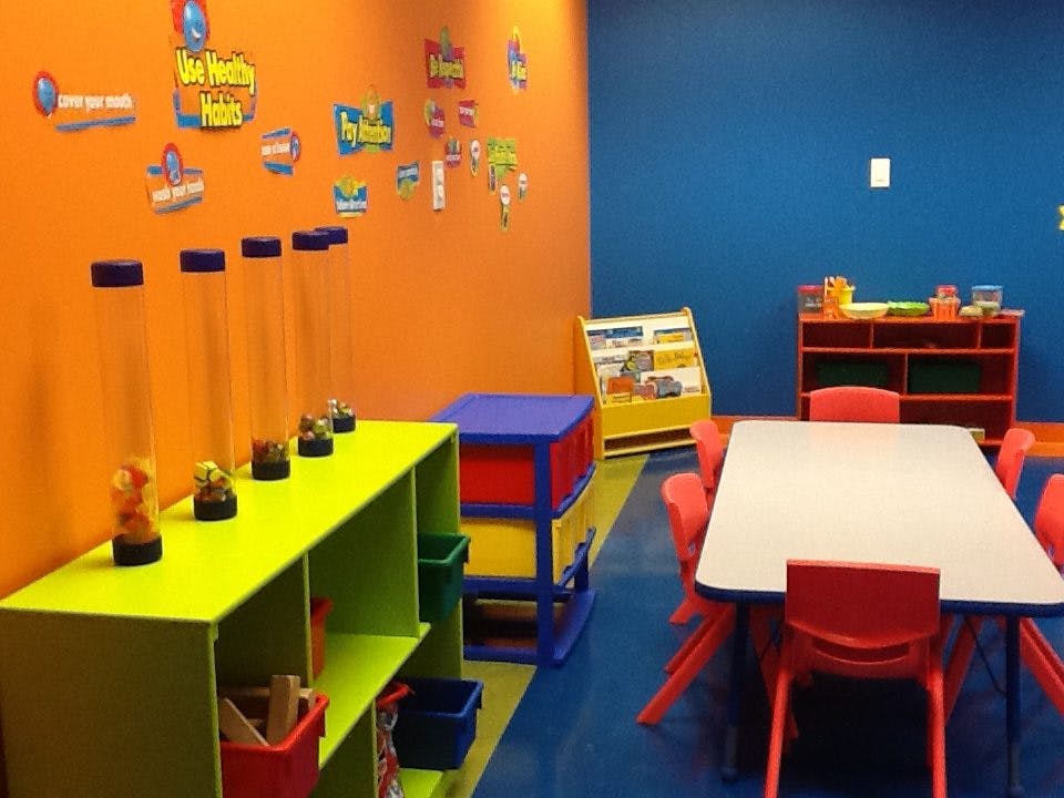 Classroom with orange and blue walls, shelves, and a table with red chairs