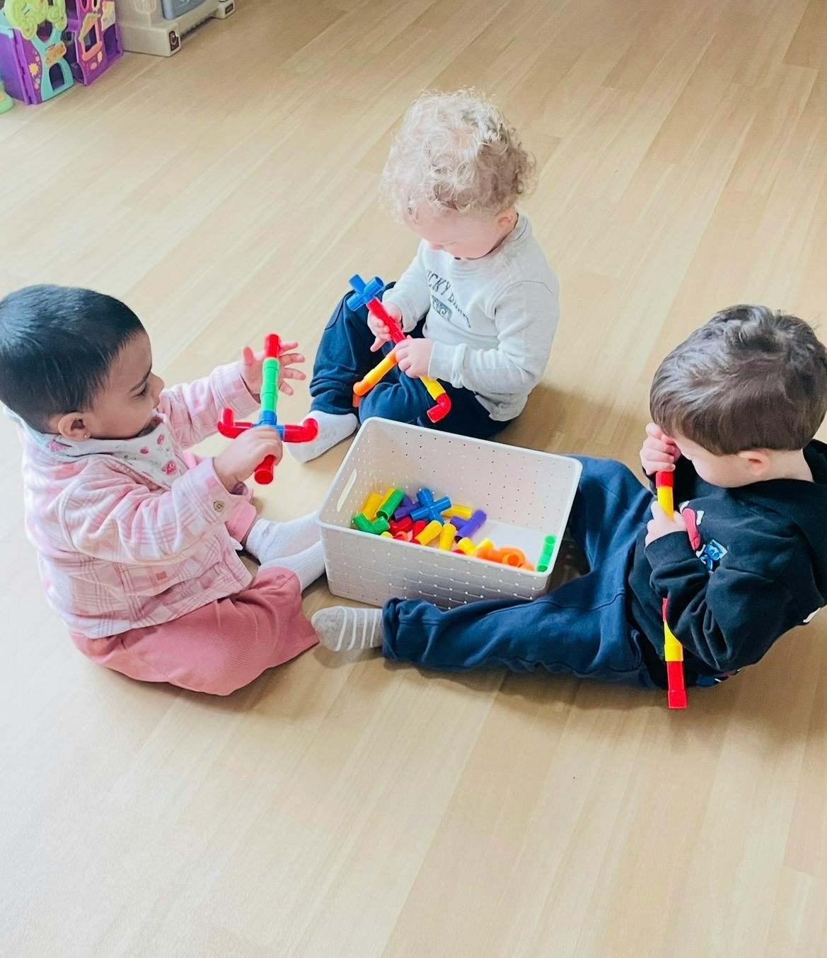 Three children sitting on the floor playing with colorful building toys