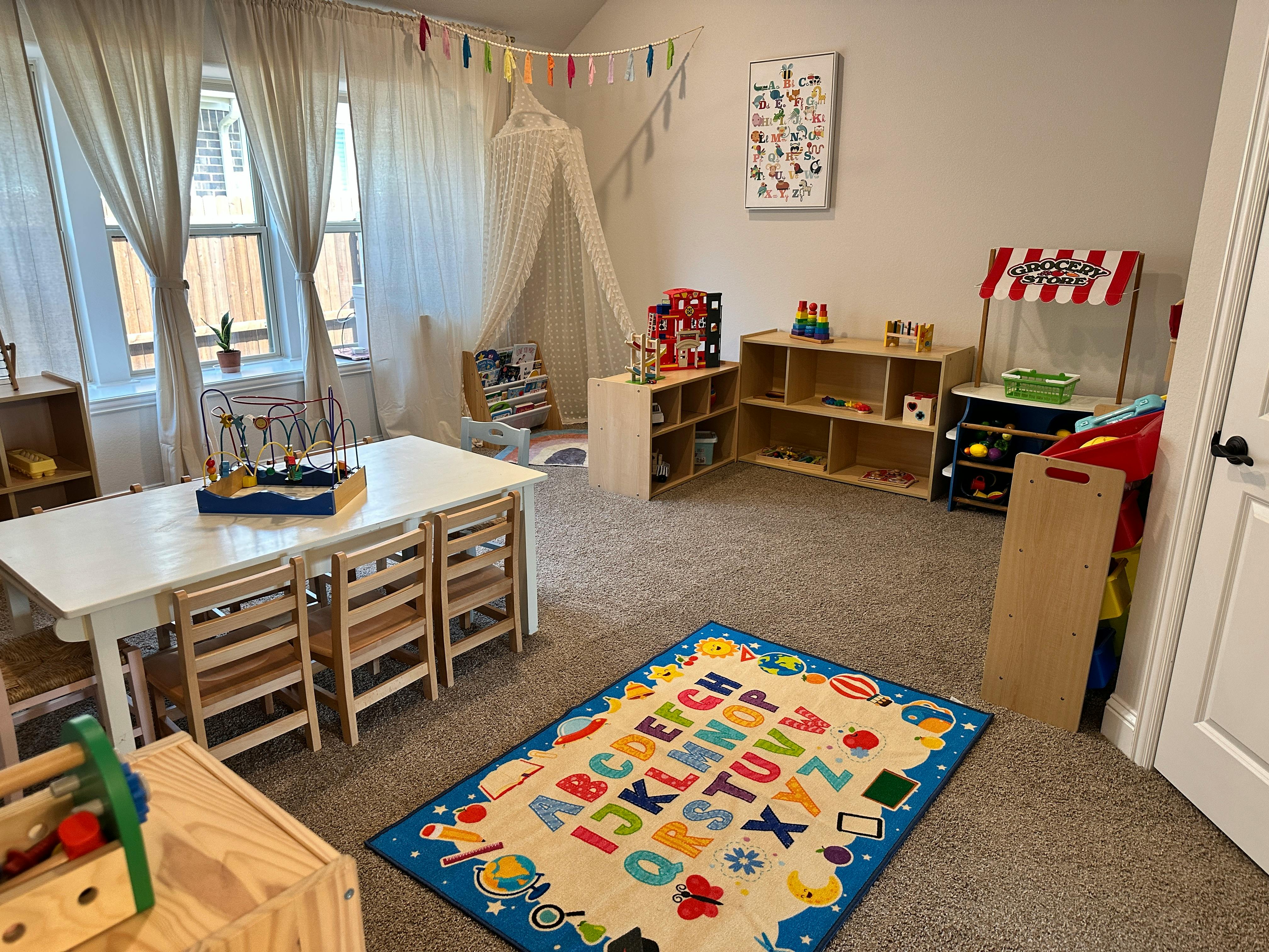 Children's play area with a table and chairs, shelves with toys, and an alphabet rug