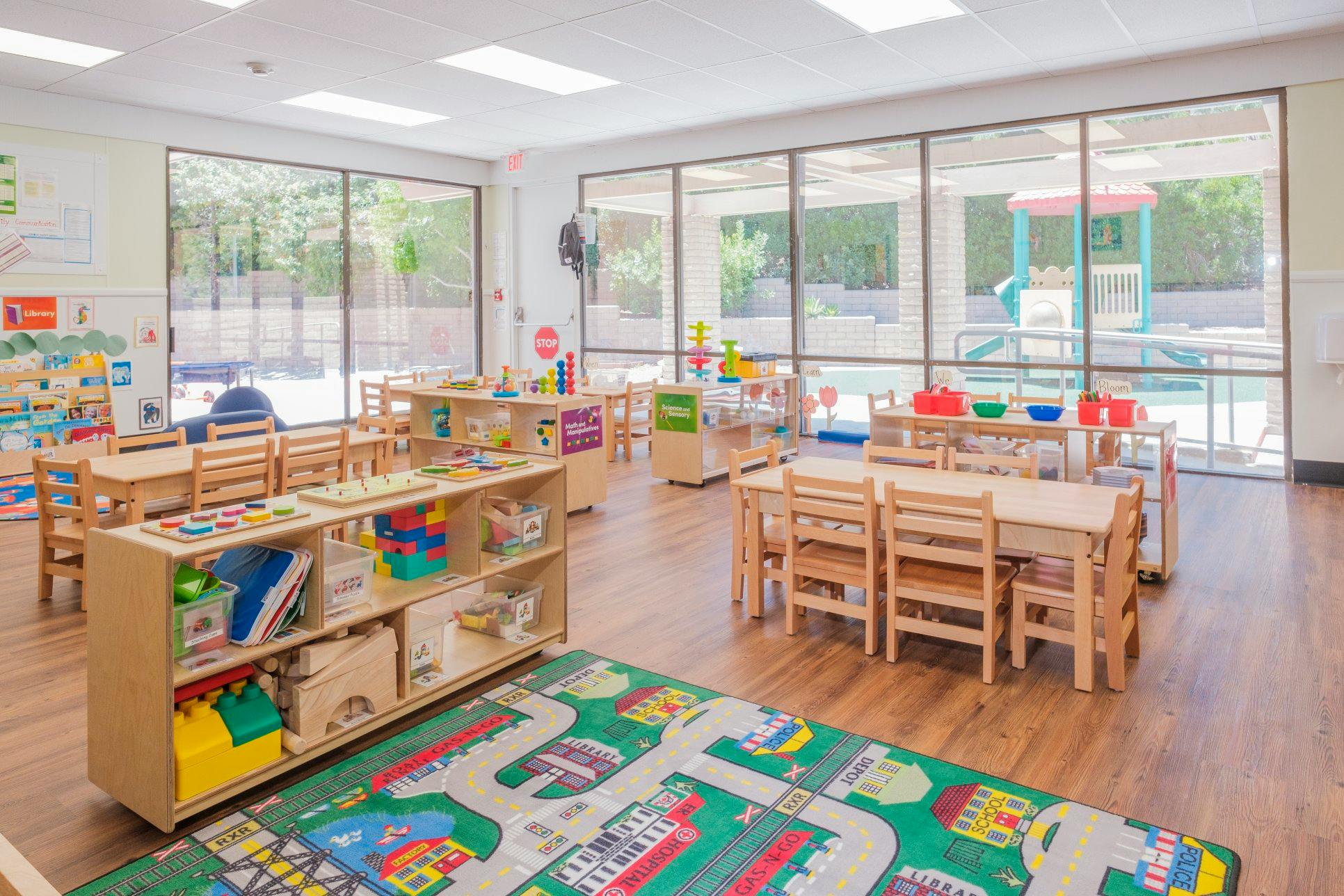 Empty colorful preschool classroom with small tables and chairs, toys, and activity rug