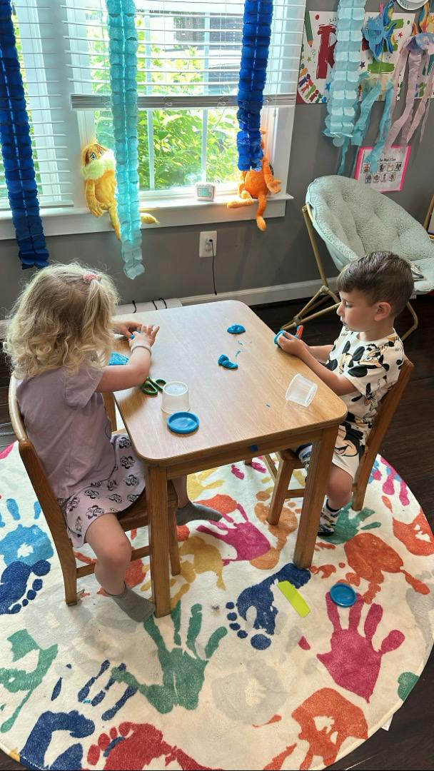Two children sitting at a table playing with modeling clay