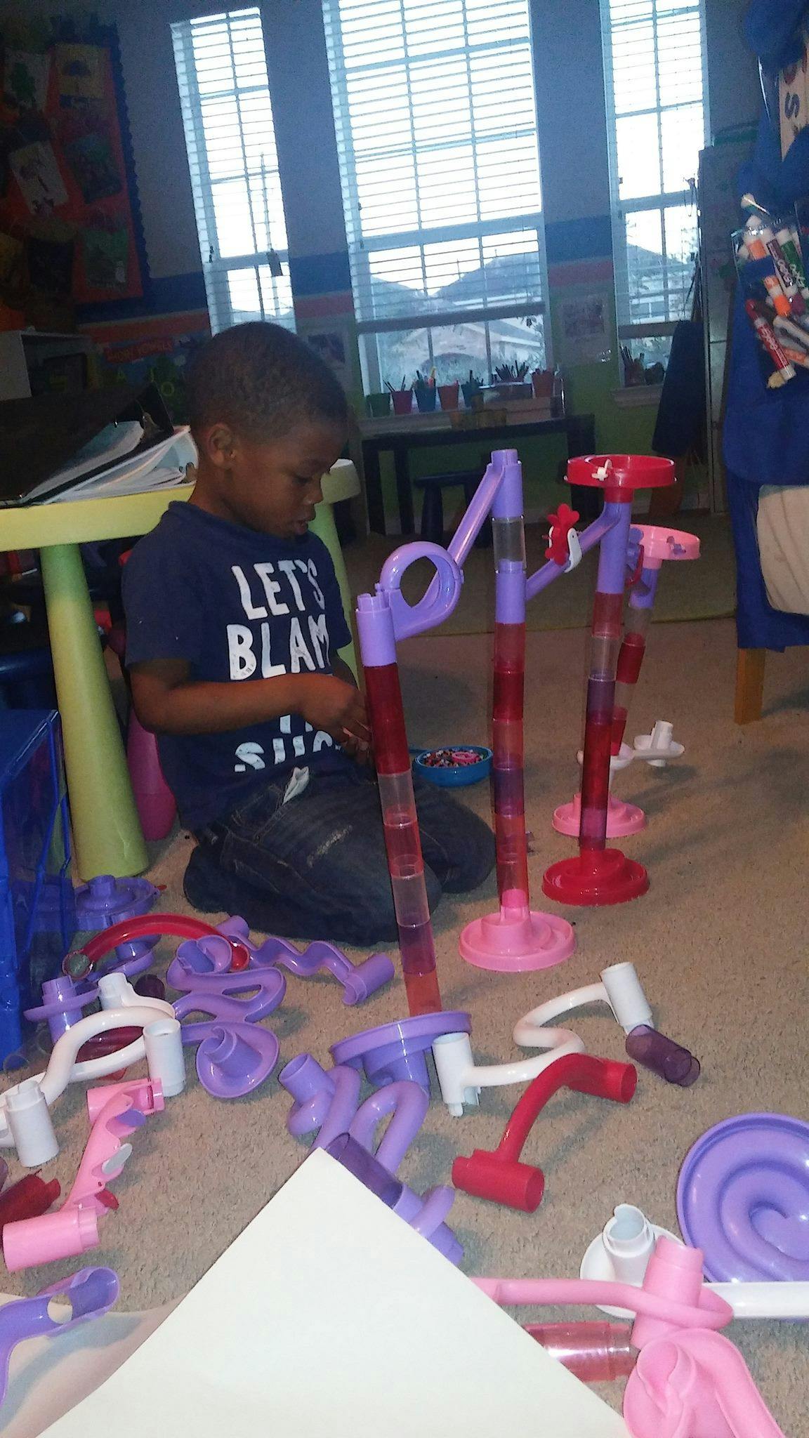 Child kneeling on floor playing with a marble run toy