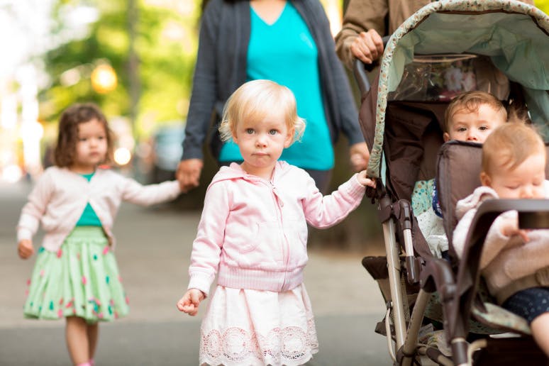Two children walking with a person pushing a stroller with two babies