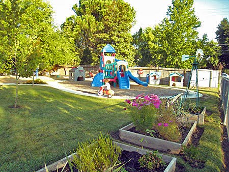 Child on a tricycle near a playground structure in a grassy yard