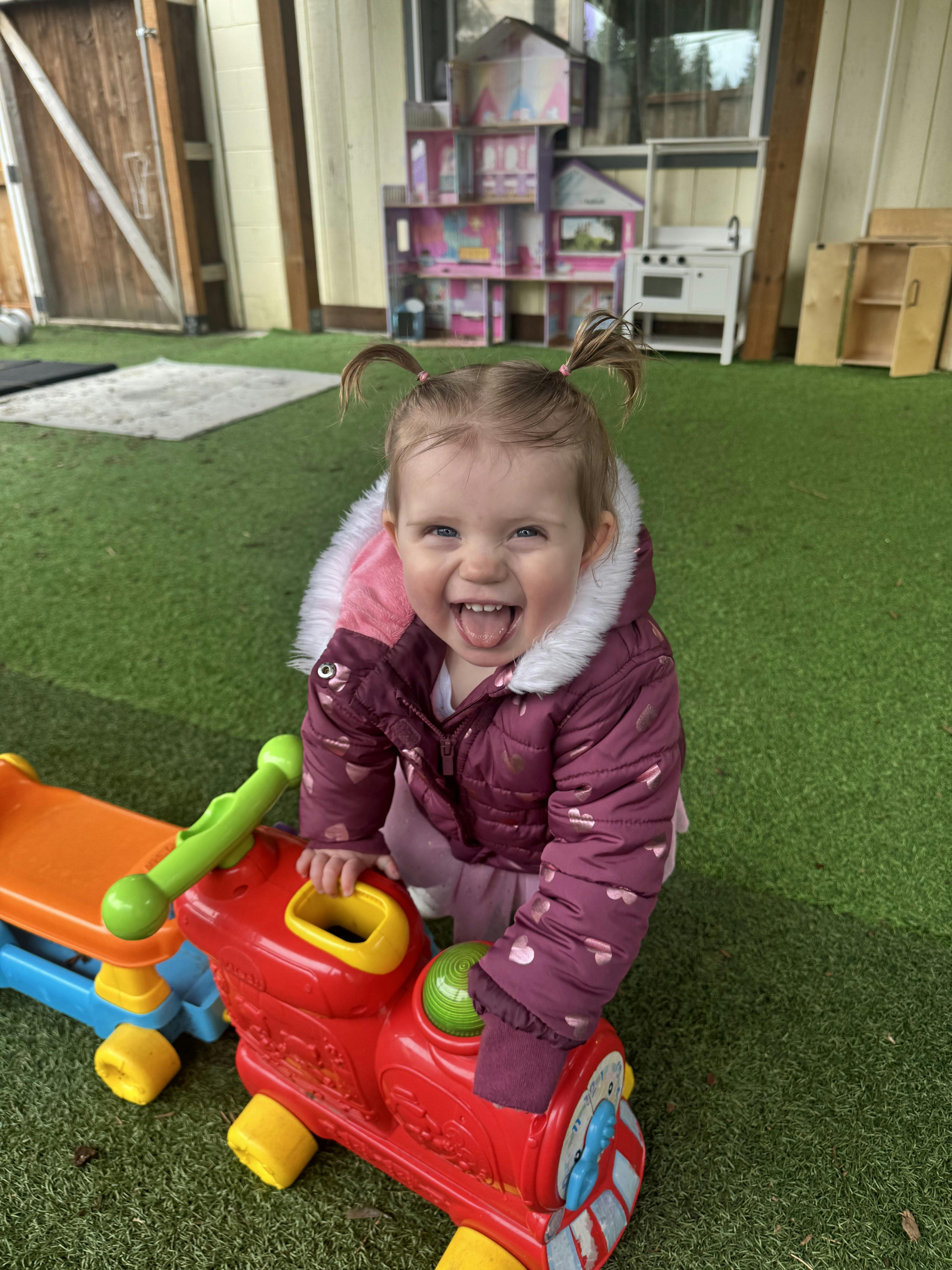 Smiling child with hair in pigtails playing with a toy train outdoors