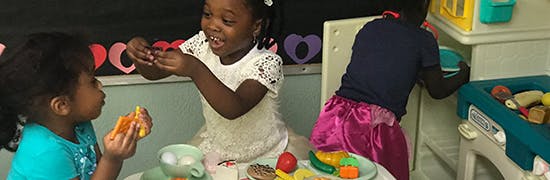 Three children playing with toy food and dishes