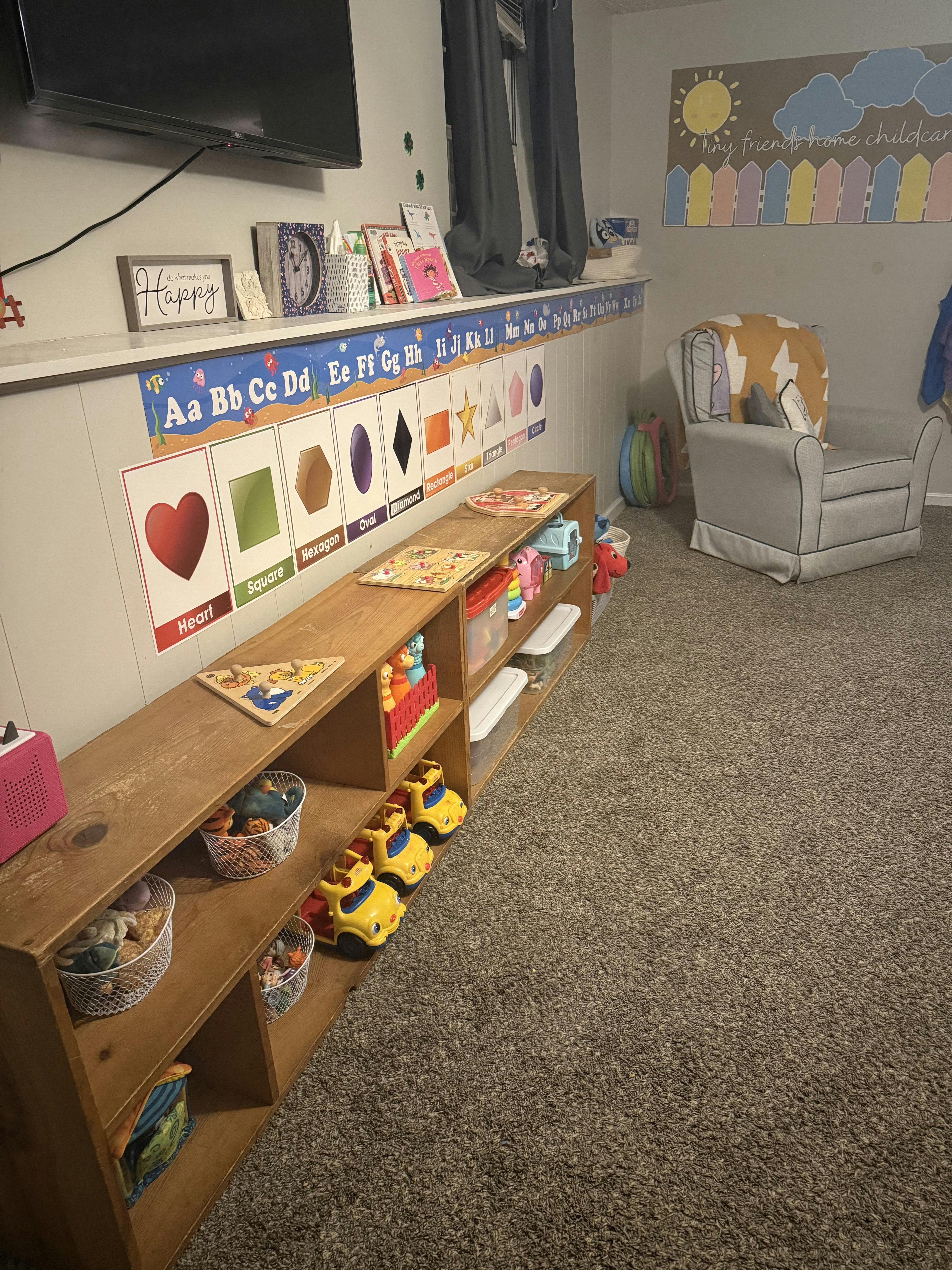 Classroom with alphabet and shape charts, toy shelves, and an armchair