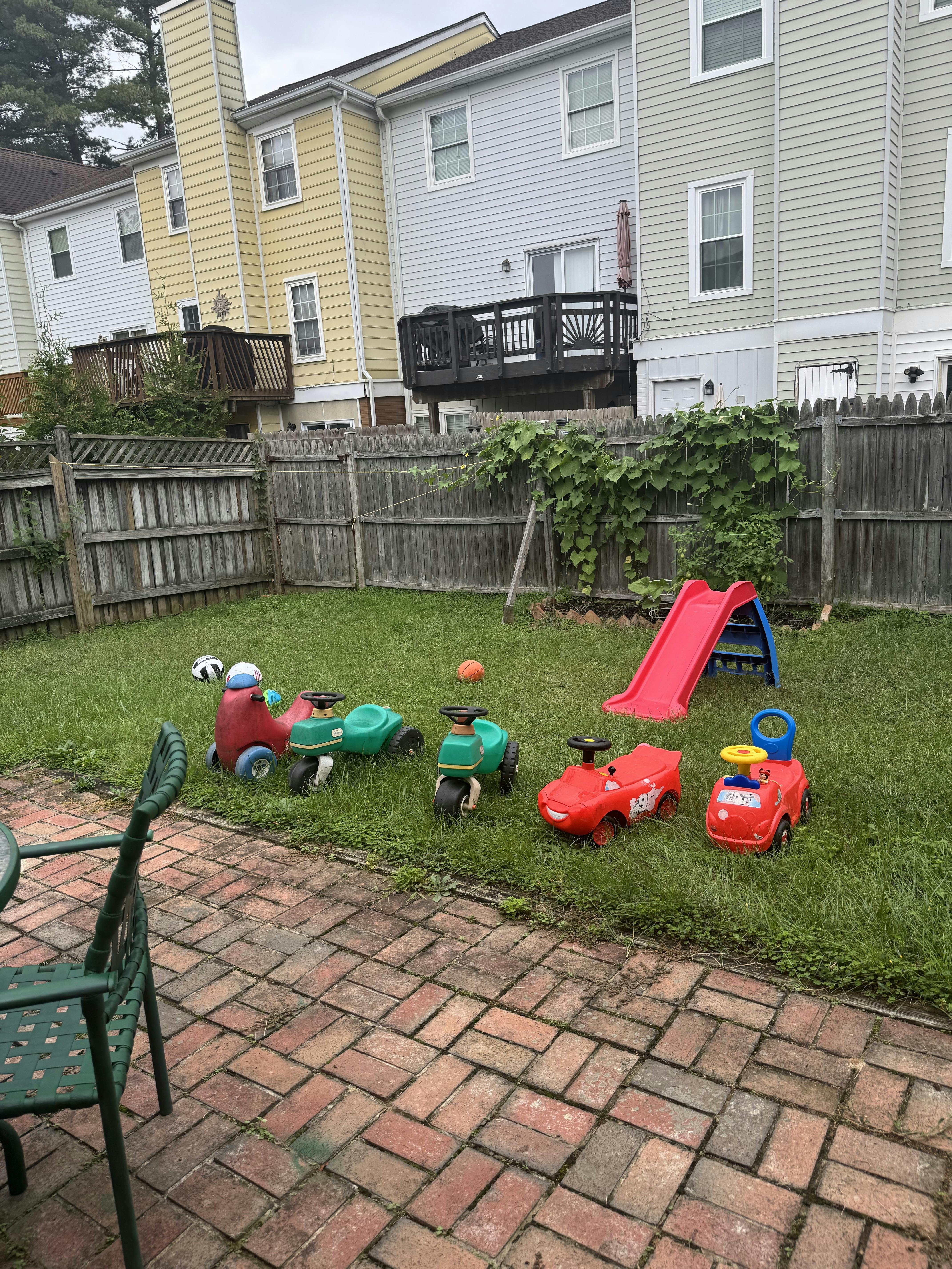 Toy ride-on vehicles and a red slide in a grassy backyard