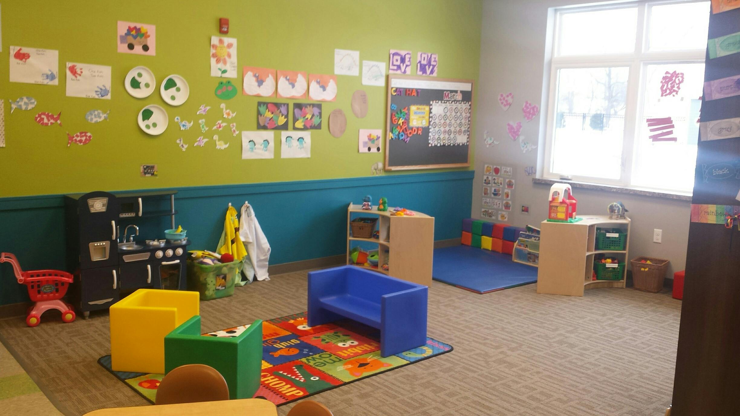 Playroom with colorful rug, small furniture, and children's artwork on walls