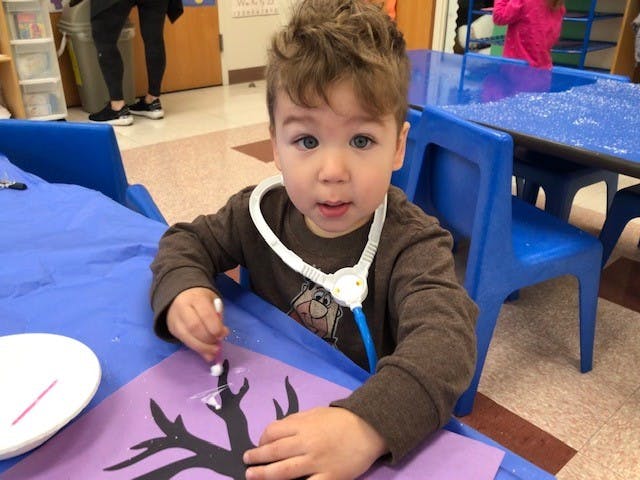 Child wearing a toy stethoscope and working on a craft project