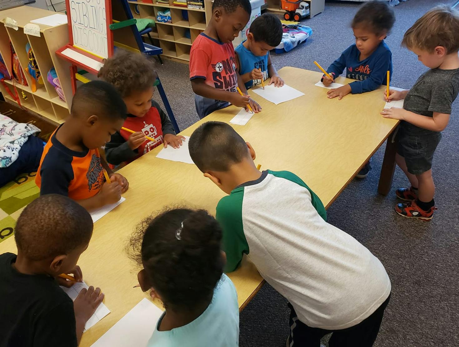 Children writing at a table in a classroom