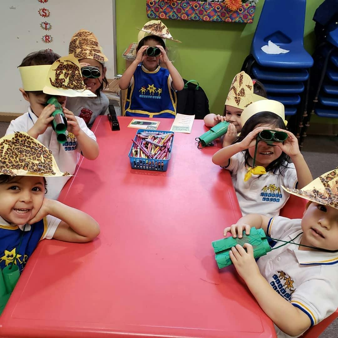 Children wearing safari hats and looking through toy binoculars at a table