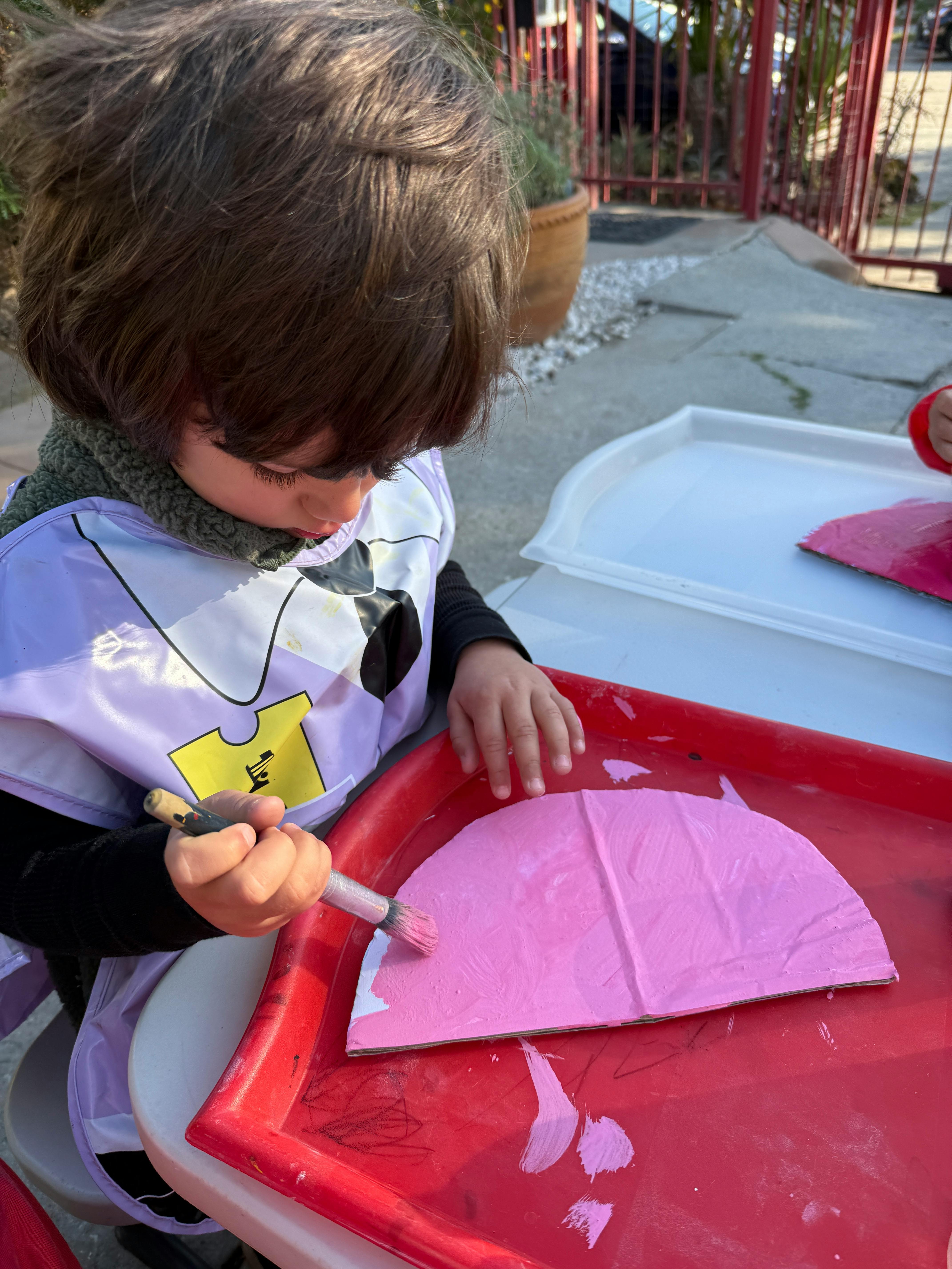 Child painting a pink shape with a brush