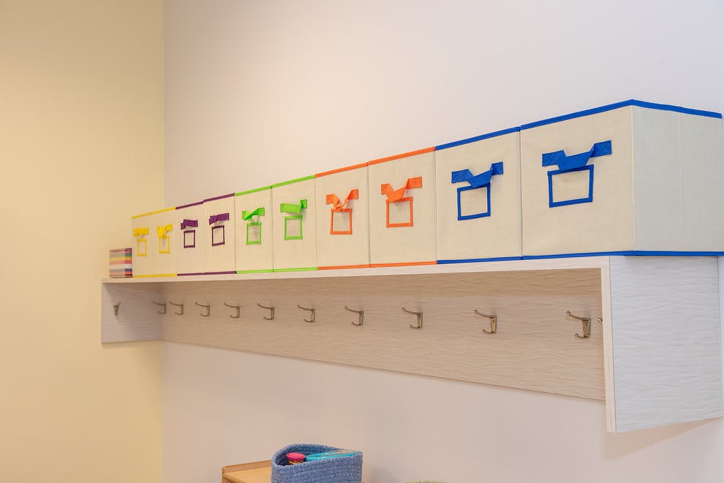 Row of colorful storage boxes on a shelf above coat hooks