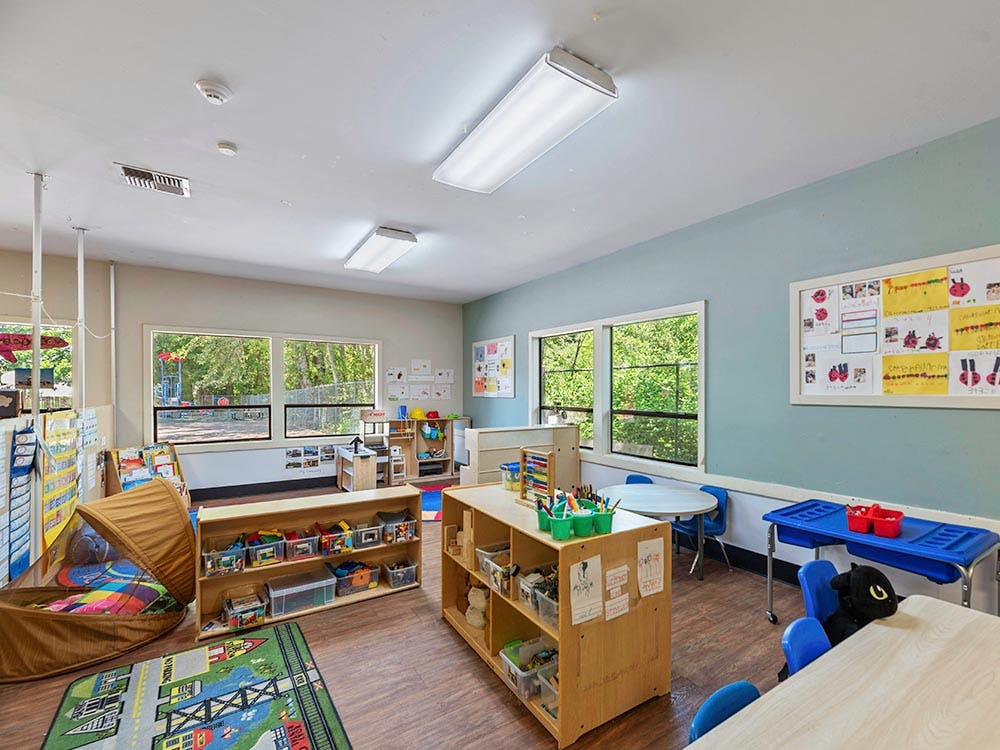 A colorful empty classroom with toys, tables, and windows looking out to a playground