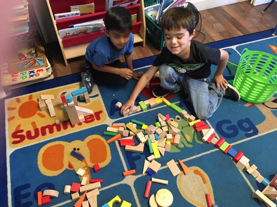 Two children playing with wooden blocks on a colorful rug