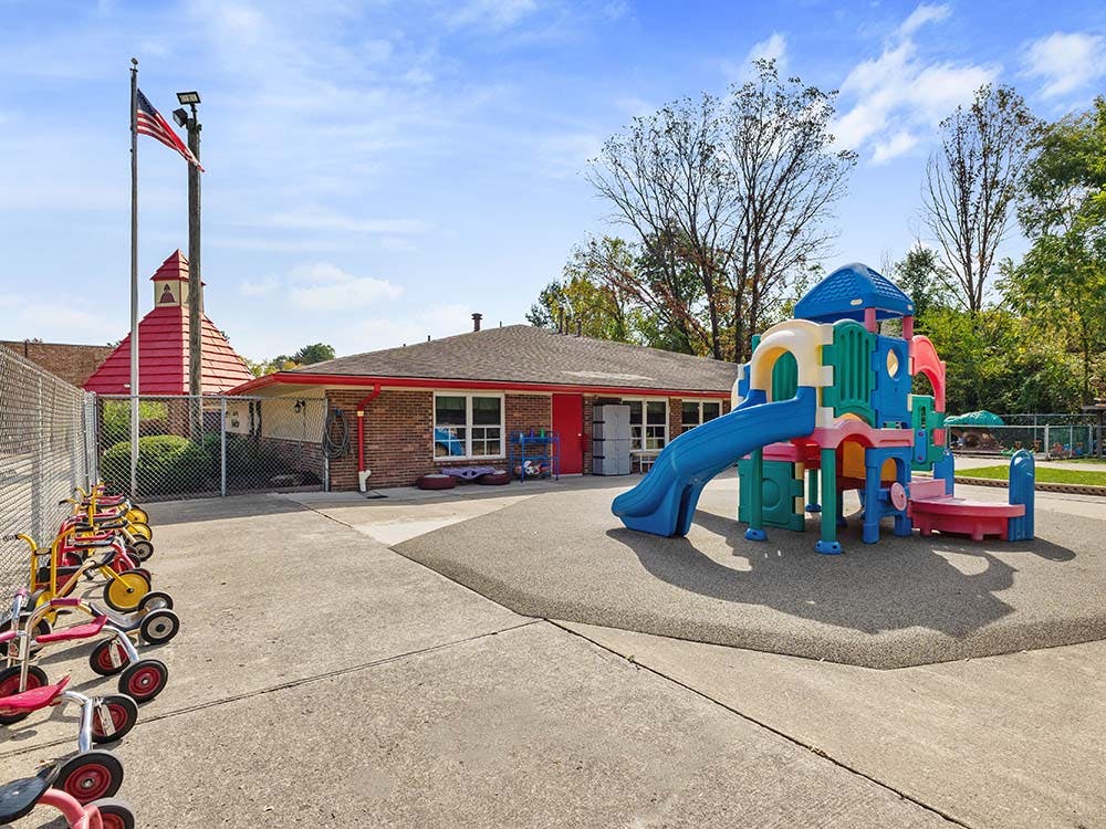 Playground with colorful slide structure and tricycles next to a building