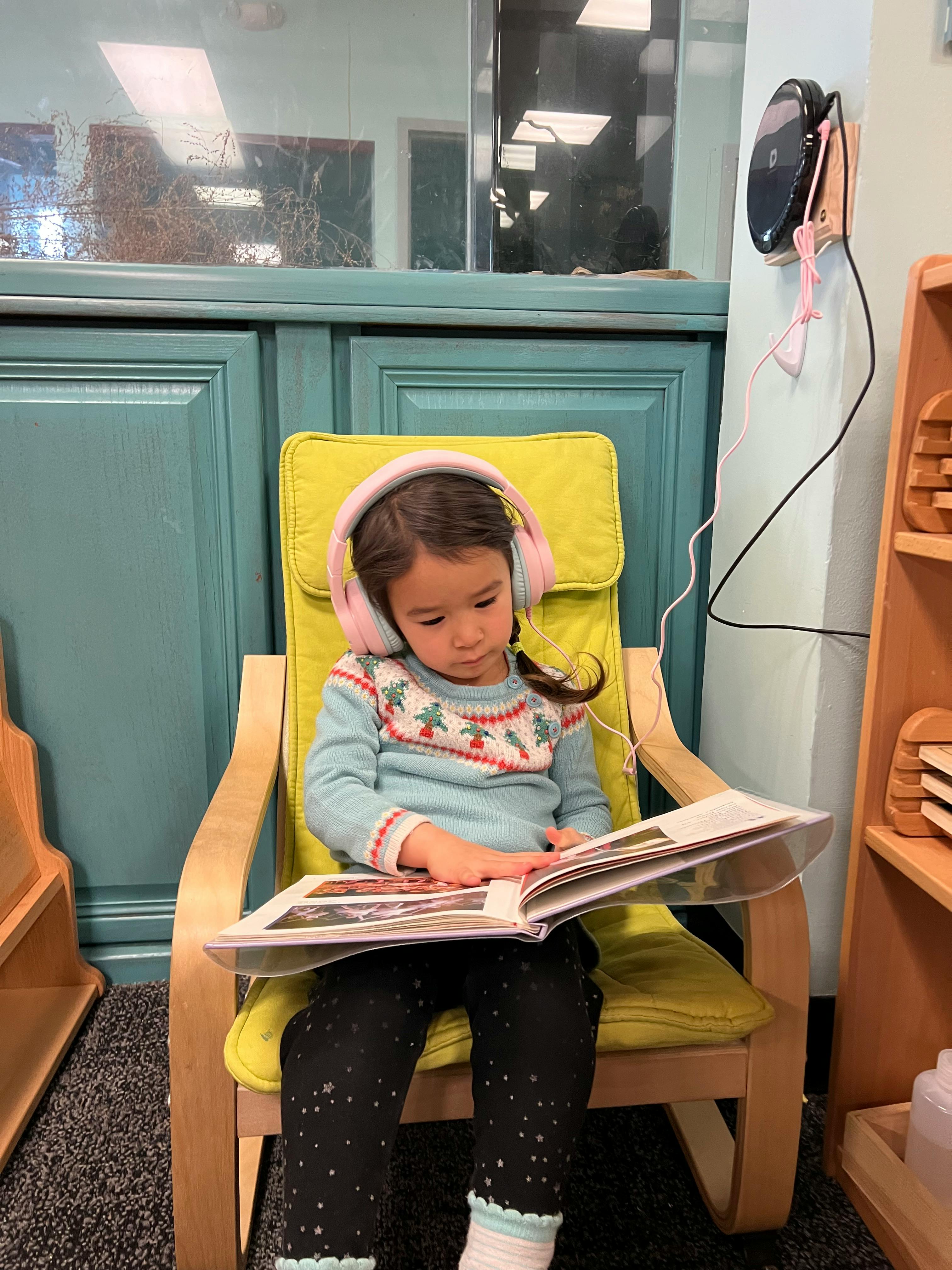 Child wearing headphones and reading a book in a chair