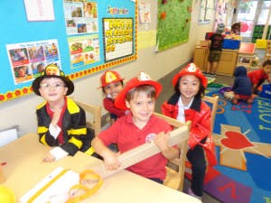 Four children in firefighter costumes in a classroom