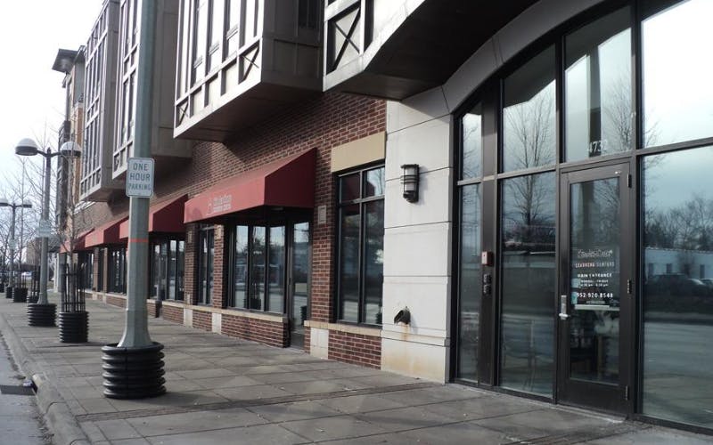 Storefronts with red awnings along a sidewalk and brick building street with a "ONE HOUR PARKING" sign