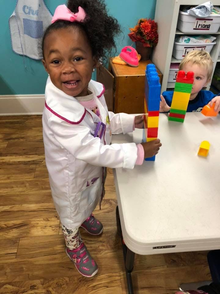 Child in a white coat playing with colorful building blocks at a table