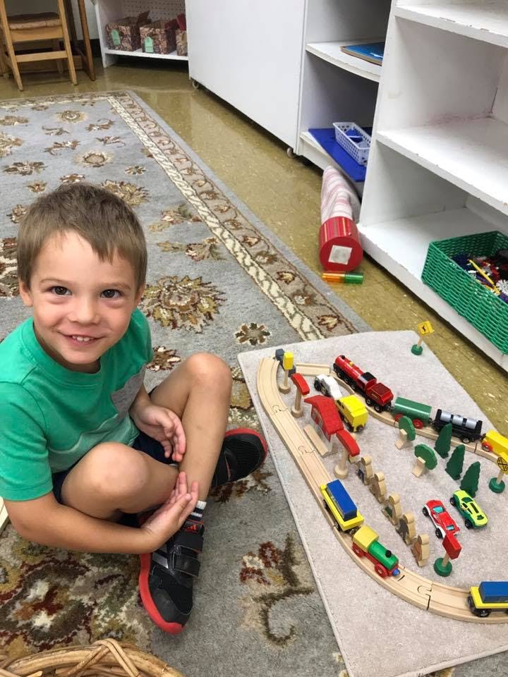 Child sitting on a rug next to a toy train set