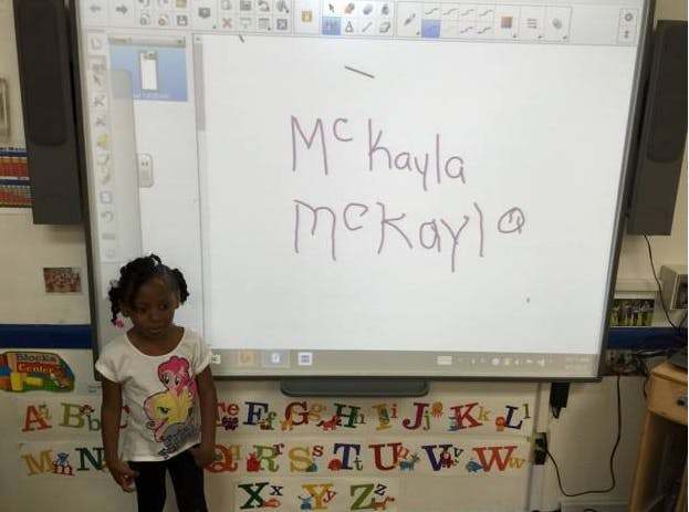 Child standing next to a whiteboard with "McKayla" written on it