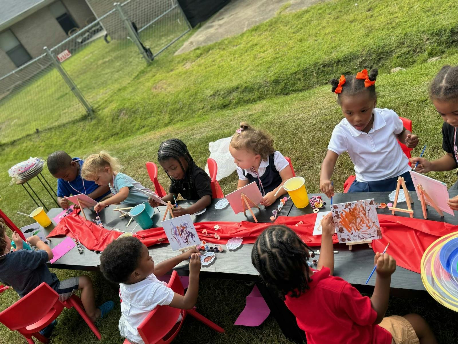 Children painting outdoors at a long table with art supplies