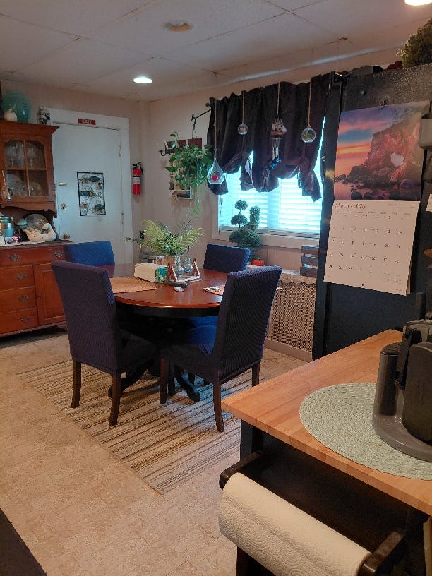 Dining room with a wooden table, dark chairs, and a calendar on the refrigerator