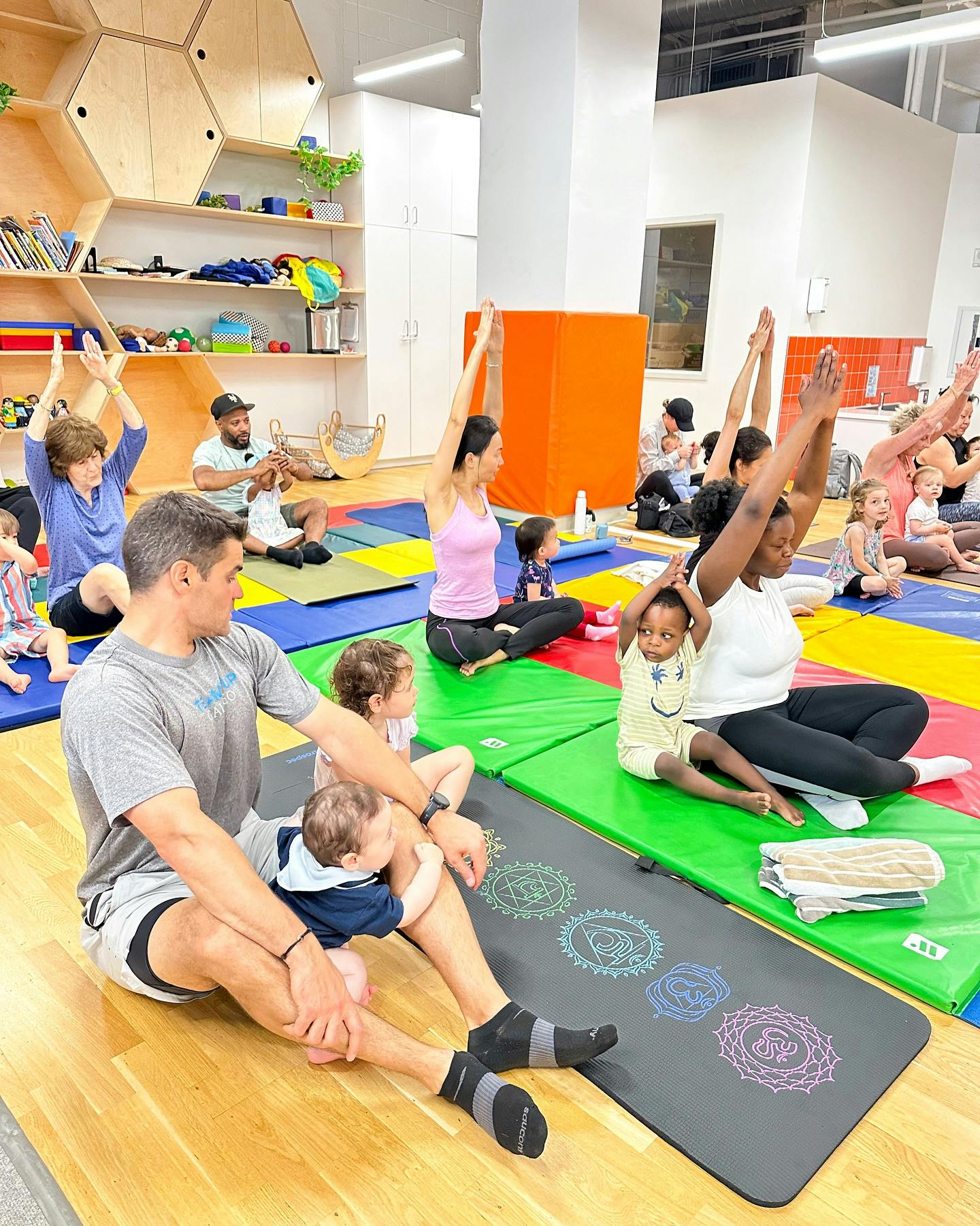 Adults and children sitting on mats with arms raised in a yoga pose