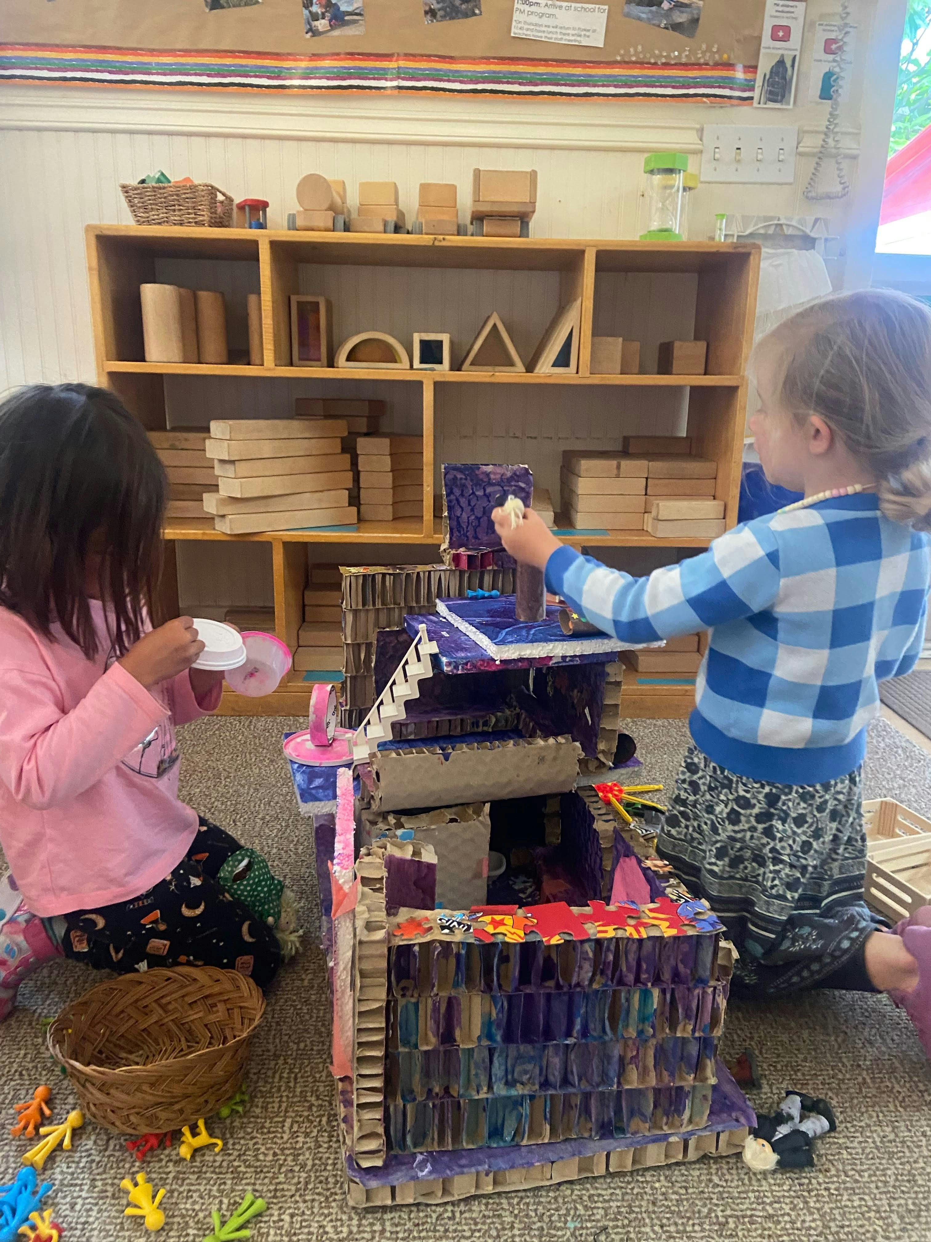 Two children playing with a large cardboard structure on the floor