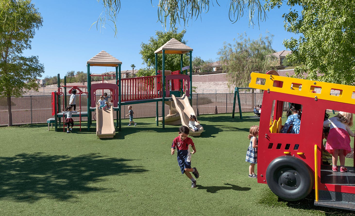 Children playing on a playground with slides, swings, and a fire truck structure
