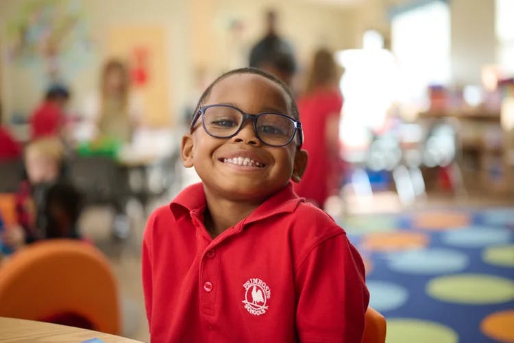 Child wearing glasses and a red shirt in a classroom