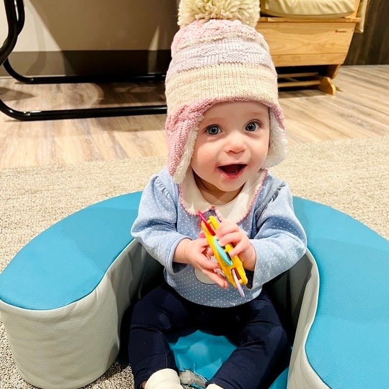 Child in a knit hat sitting in a baby seat holding a toy