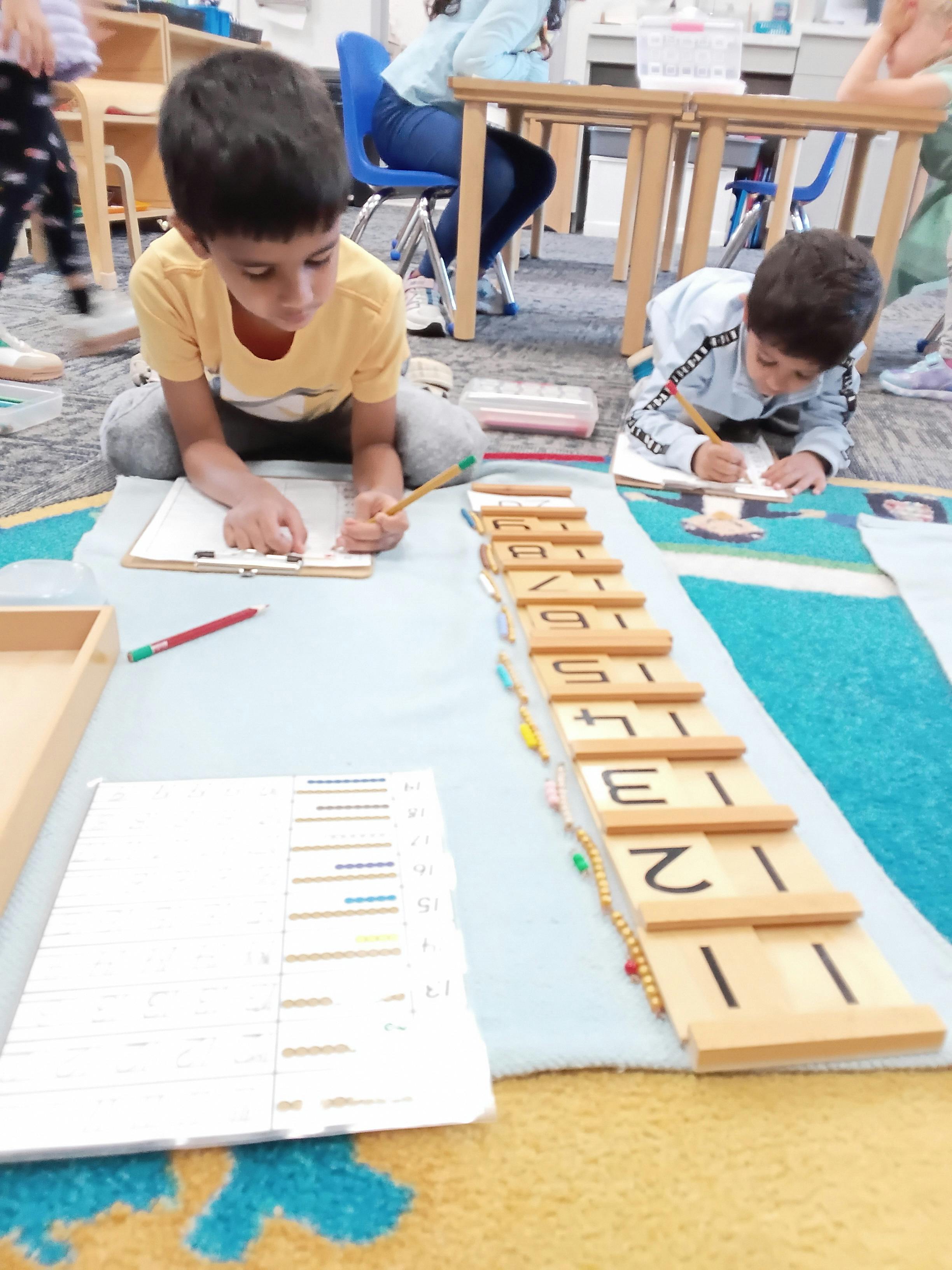 Two children writing and working with number blocks on a classroom floor