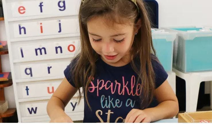 Child looking down at a surface, with an alphabet chart in the background